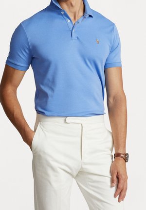 Lichtblauw poloshirt met korte mouwen met een klassieke kraag, voorzien van een klein geborduurd logo op de borst; gecombineerd met een witte broek.