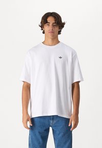 Hvid bomulds t-shirt med rund hals, korte ærmer og et lille sort logo på brystet. Løs pasform med lige kant.