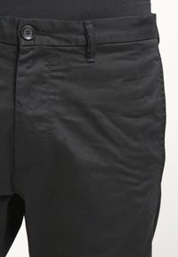 Svarta byxor av slät tyg med en enda knappstängning, diagonala sidfickor och en subtil textur utan synliga mönster.