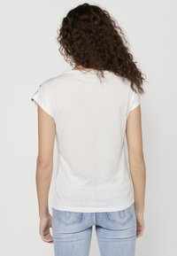 T-shirt blanc à manches courtes avec un col rond, un ourlet droit et une texture subtile. Coupe légèrement ample, associé à un jean bleu clair.