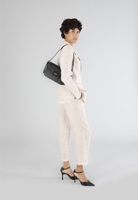 Ljust beige randig kostym med skräddarsydd passform, tillsammans med svarta spetsiga klackskor och en liten svart axelremsväska. Släta texturer genomgående.