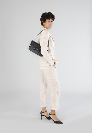 Lyse beige stribet jakkesæt med en skræddersyet pasform, parret med sorte spidse hæle og en lille sort crossbody taske. Glatte teksturer hele vejen igennem.