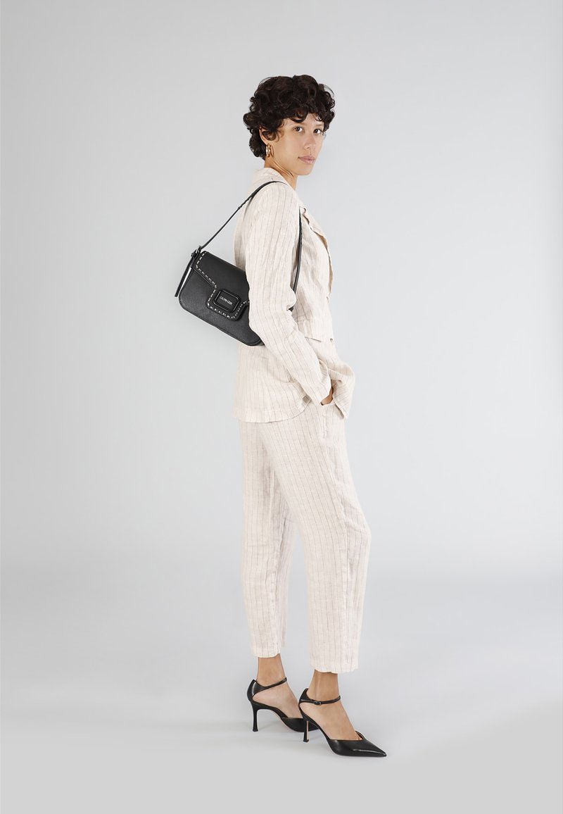 Ljust beige randig kostym med skräddarsydd passform, tillsammans med svarta spetsiga klackskor och en liten svart axelremsväska. Släta texturer genomgående.