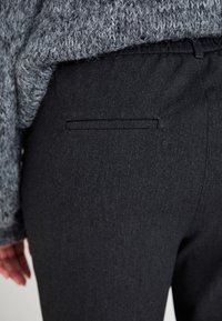 Pantalones negros de textura suave, con cinturilla elástica y un bolsillo trasero. La tela parece ser duradera y ligeramente texturada.