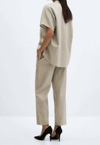 Top en lin beige à manches courtes, associé à un pantalon assorti et des escarpins noirs à bout pointu. La tenue présente une coupe décontractée et un design simple.