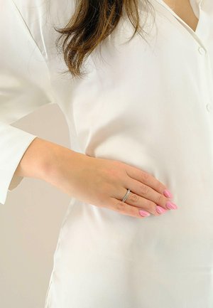 Blusa bianca di raso con un ampio colletto. Una mano con un anello d'argento e unghie rosa allungate poggia sul tessuto, mettendo in mostra la sua morbidezze.