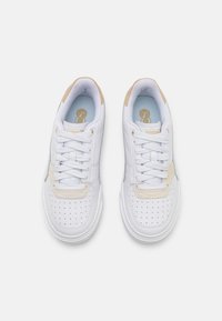 Białe trampki z gładką skórzaną cholewką, perforowanym czubkiem, beżowymi zamszowymi akcentami i białymi sznurowadłami. Wewnątrz widoczne jasnoniebieskie wkładki.