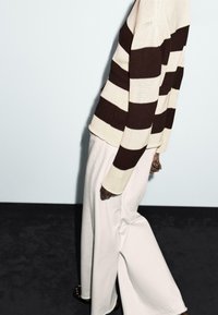 Knitted sweater with brown and cream vertical stripes, paired with wide-legged white pants. Textured fabric and relaxed fit.
