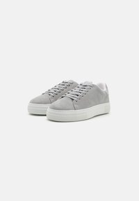Szürke velúr sneaker fehér gumitalppal, lekerekített orral, fűzős kialakítással és texturált felsőrészsel. Minimalista stílus tiszta vonalakkal.