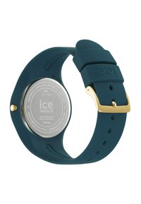 Montre en caoutchouc avec un bracelet teal, matériel doré, boîtier rond et dos en argent. Dispose d'un design minimaliste et d'une résistance à l'eau jusqu'à 10 ATM.
