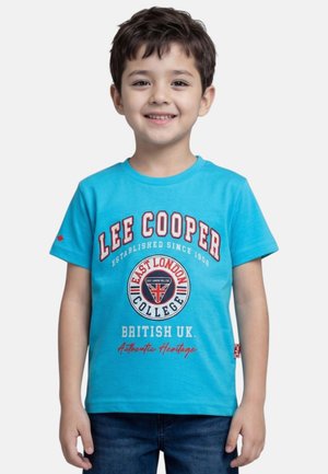 Garçon souriant portant un t-shirt bleu Lee Cooper avec le logo "East London College" et le drapeau britannique, associé à un jean bleu foncé.