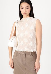 Top sem mangas de renda em branco com bordado floral, combinado com uma saia ajustada castanha. O modelo carrega uma pequena bolsa branca.