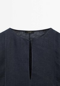 Top in lino blu scuro con scollatura rotonda e dettaglio a chiave sul davanti. Il tessuto ha una sottile texture e cade leggero.