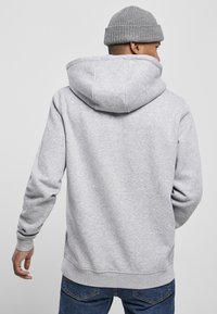 Grå hoodie i blødt stof med en stor hætte og ribbede manchetter. Båret over navy jeans, der har et enkelt, afslappet design.