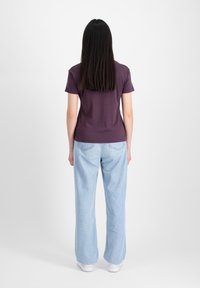 Kortærmet, tætsiddende, lilla T-shirt parret med lyseblå, brede jeans; model der bærer hvide sneakers, set fra ryggen.