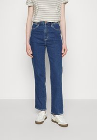 Mörkblå högmidjade jeans med raka ben, fem fickor och kontrasterande sömmar. Kombineras med en randig kortärmad topp och sneakers.