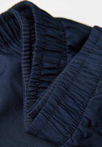 Námořnická modrá oděv s nařaseným elastickým pasem. Hladká textura s matným povrchem, s prošitými akcenty podél okrajů.