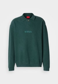 Tume roheline dressipluus polo kaelusega, millel on rinna peal broderitud "HUGO" logo ja soonikkoes varrukate ning hem.