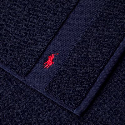 Serviettes de bain en coton bleu marine, présentant une surface texturée et un logo polo brodé rouge dans un coin. Matière douce et épaisse, forme rectangulaire.