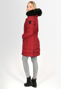 Red padded coat with a black faux fur hood, zipper pockets, and a slightly fitted design. Paired with gray skinny jeans and black boots.