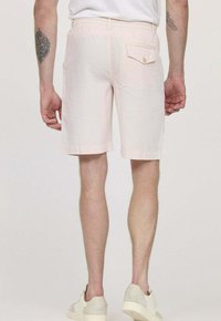 Shorts rose clair en tissu doux, avec une poche arrière dotée d'un détail boutonné. L'ourlet est droit et se termine au-dessus du genou.