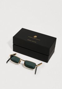 Črne pravokotne sončne očali z zlatimi okvirji, postavljene ob črno škatlo, označeno z "Očala Davida Beckhama, posebna izdaja."