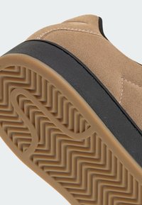 Semišová teniska v hnedej farbe s čiernou gumovou podrážkou. Na podrážke je detailný vzor rybej kosti a na vrchu kontrastné šitie.