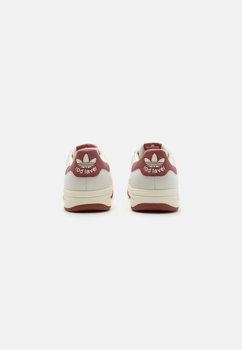 Baskets blanches avec des accents bordeaux, tige texturée, talon rembourré et logo signature au dos. Semelle en caoutchouc avec un motif de bande de roulement distinct.