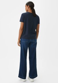 Marineblaues Baumwoll-T-Shirt mit kurzen Ärmeln, kombiniert mit weit geschnittenen blauen Jeans. Die Jeans haben einen geraden Schnitt und dezente Nähte.