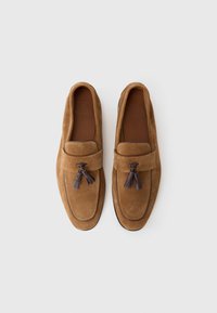 Hnedé semišové loafers s plochou podrážkou, so dekoratívnym strapcom a prešitím pozdĺž okraja. Hladká vnútorná podšívka.