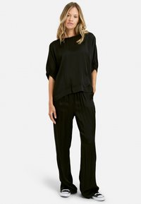 Top negro holgado con mangas anchas, combinado con pantalones negros sueltos. Ambos tienen una textura suave y satinada con un brillo sutil. Zapatillas blancas.