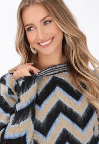 Daugiaspalvis chevron rašto megztinis, turintis juodas, mėlynas ir kremines juostas, pagamintas iš minkštos, pūkuotos medžiagos su įranga apykakle.