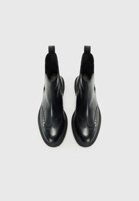 Bottines en cuir noir à bout rond, avec des détails de brogue décoratifs et des tirants pour un enfilage facile. Texture lisse avec une semelle robuste.