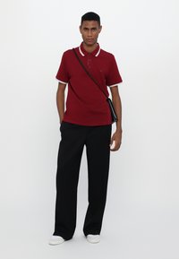 Rød polo skjorte med hvit kant, med klassisk krage og tre knapper, kombinert med svarte vide bukser og hvite joggesko.