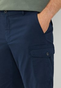 Pantaloni cargo blu realizzati in misto cotone, con una tasca laterale con chiusura a bottone e una vestibilità comoda. Tessuto testurizzato con finitura liscia.
