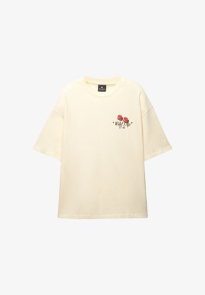 Krem majica preko veličine izrađena od mekanog pamuka; sadrži cvjetni grafički uzorak u crvenoj i crnoj boji s lijeve strane. Kratki rukavi, okrugli izrez.