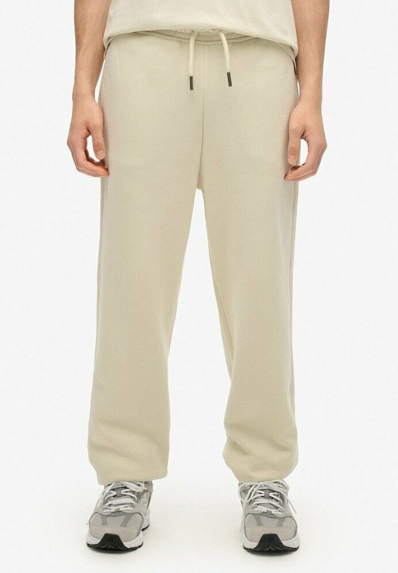 Lichtbeige joggingbroek in een relaxed fit, met een elastische tailleband en trekkoord, en twee zijzakken. Gecombineerd met grijze sneakers.