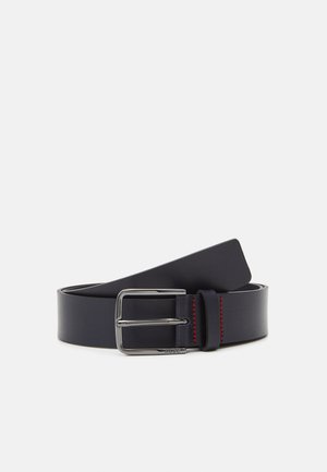 Ceinture en cuir bleu marine avec une texture lisse, dotée d'une boucle en métal argenté et d'un détail de couture rouge sur le bord.