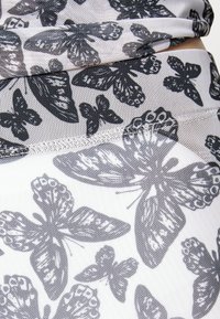 Leggings brancos com um padrão de borboleta preta, feitos de um material suave e texturizado, e um design sem emendas na cintura.