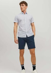 Cămașă cu mâneci scurte, de culoare albastru deschis, cu un model geometric multicolor. Asociată cu șorturi de culoare albastru închis și adidași albi.