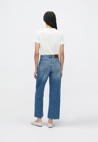 Modré džíny s vysokým pasem a rovnými nohavicemi, které jsou na stehnech vybledlé. Mají zadní kapsy a hnědou koženou nášivku s logem na pásku.