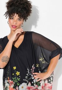 Blusa kimono nera con maniche trasparenti, caratterizzata da un colletto a V e una stampa colorata di fiori rosa e gialli all'orlo.