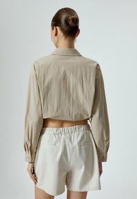 Beige cropped shirt met lange mouwen en kraag, gecombineerd met witte high-waisted shorts met elastische tailleband en twee achterzakken.