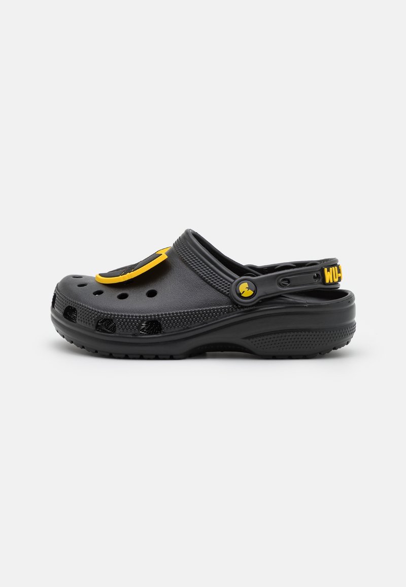 Sabots noirs avec une touche de jaune, en matériau durable, dotés de trous de ventilation, d'une sangle arrière et de zones texturées surélevées pour une meilleure adhérence.