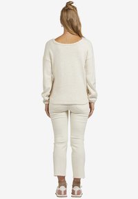 Cremiger Pullover mit weicher Textur, weitem Ausschnitt und überschnittenen Schultern. Kombiniert mit weißen, verkürzten Jeans und hellen Sneakers.