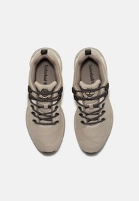 Zapatillas deportivas grises con un upper de malla texturada, cordones negros y un logo visible en la lengüeta. Punta redondeada y estructura de soporte.