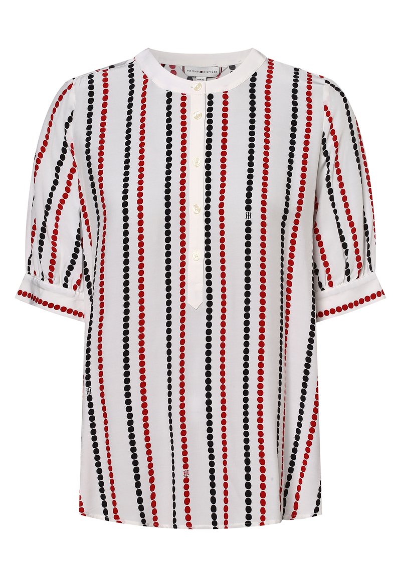 Blusa bianca con strisce verticali rosse e nere e pois, caratterizzata da un colletto rotondo e bottoni sulla parte anteriore. Maniche corte a sbuffo.