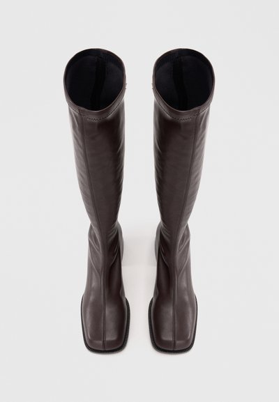 Botine din piele maro, până la genunchi, cu un design elegant, vârf pătrat și cusături subtile pe margini. Textură netedă cu o siluetă ajustată.