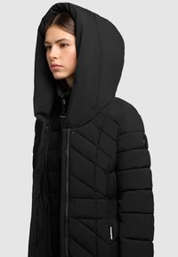 Zwarte gewatteerde jas met een grote capuchon, voorzien van een diamantgestikt textuur, een rits aan de voorkant en een logo-label aan de zijkant.