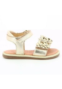 Sandale métallisée dorée avec accents floraux et strass, sangle ajustable, dos ouvert et semelle plate, équipée d'une semelle intérieure rembourrée beige.